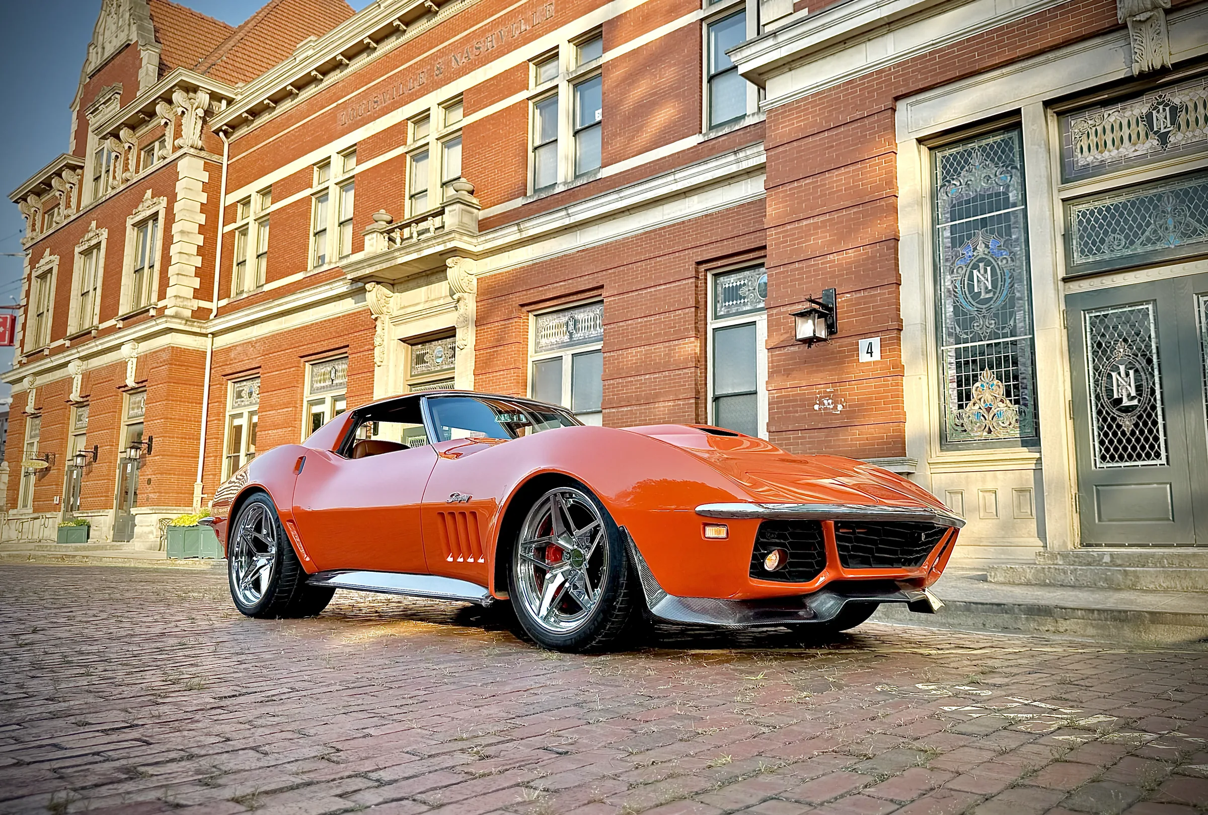 Orange classic Corvette in a street setting, front three-quarter view.