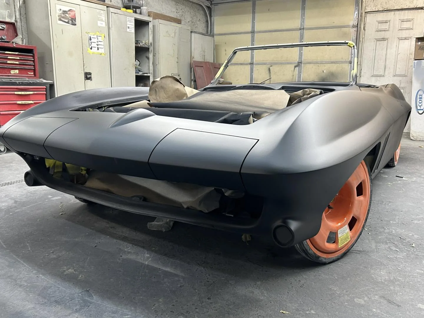 C2 Corvette convertible body in primer with stinger hood and orange transport wheels.