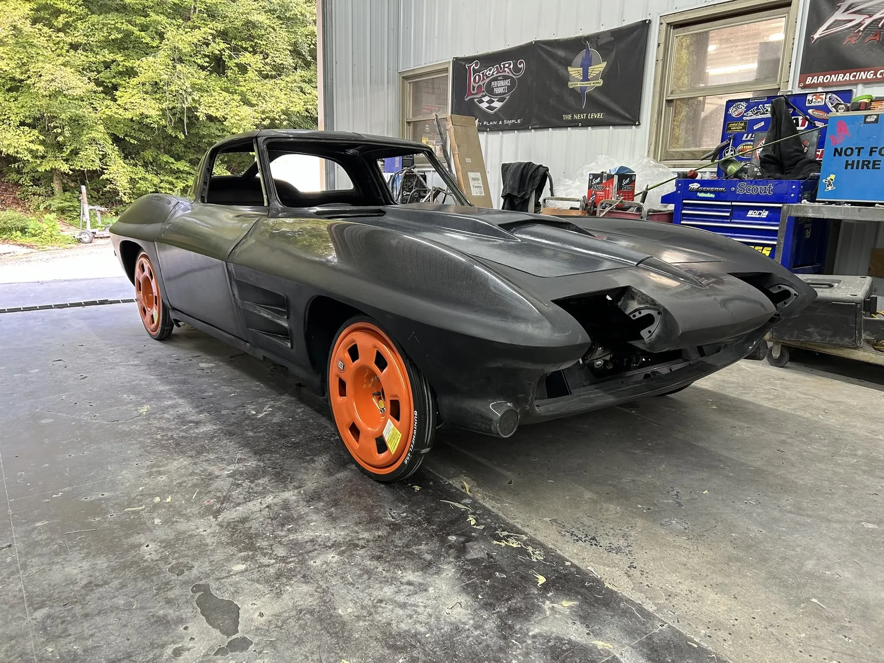 C2 Corvette split-window coupe composite body shell on transport wheels in shop bay.