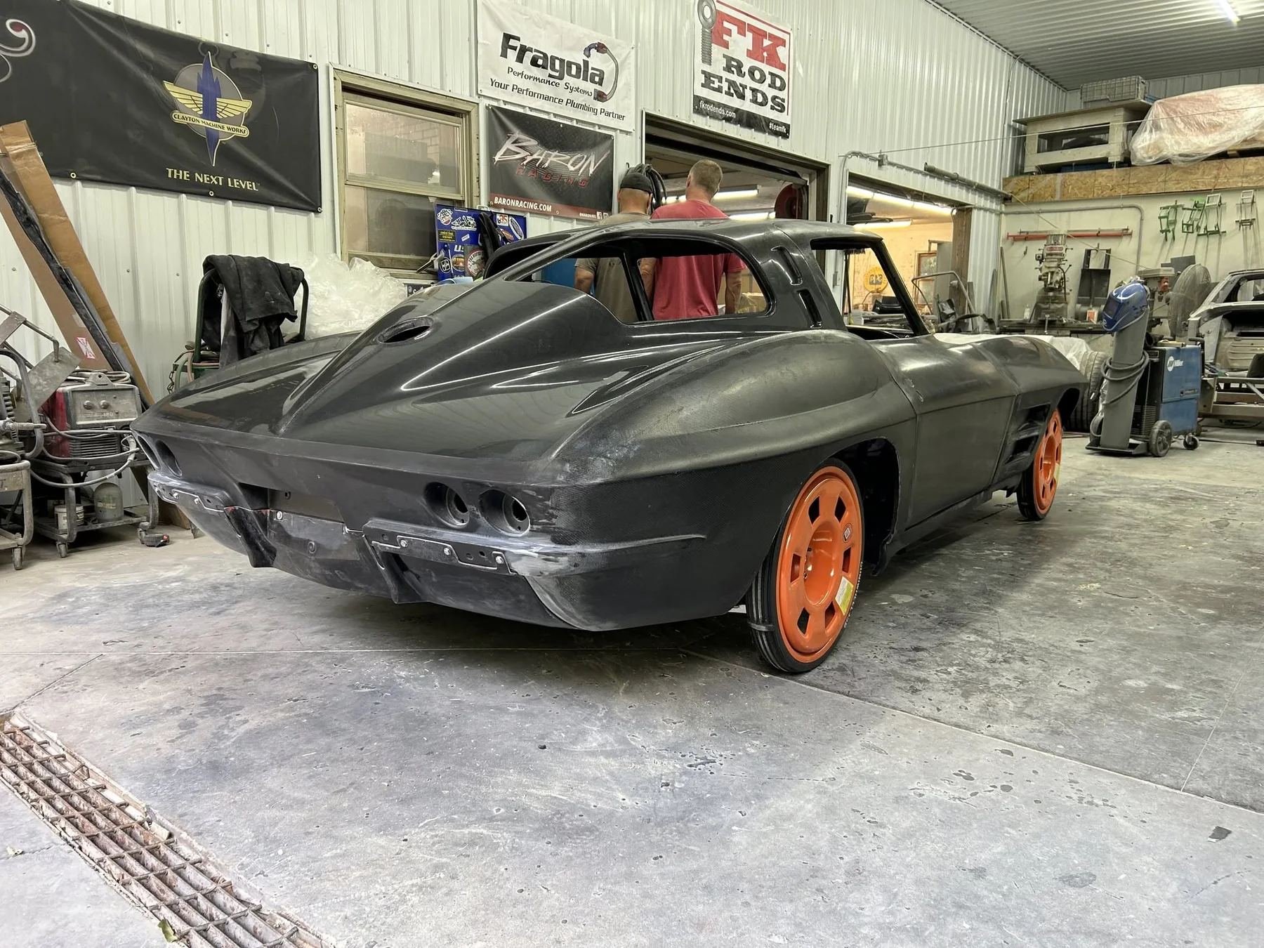 C2 Corvette split-window composite body shell rear three-quarter view with orange transport wheels in workshop bay.