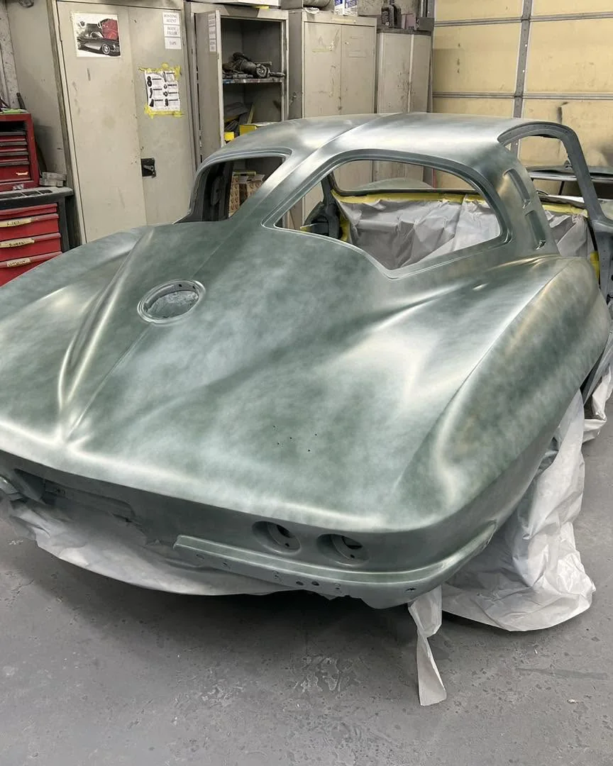 Classic C2 split-window coupe body shell in primer inside the workshop.